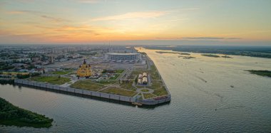 Arka planda büyük bir su kütlesi olan bir şehir. Su teknelerle dolu ve gökyüzü turuncu ve pembe. Nizhny Novgorod