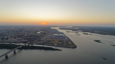 Nehir akan bir şehir ve su üzerinde bir köprü. Gökyüzü turuncu ve güneş batıyor. Nizhny Novgorod