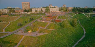 Arkasında bir tepe ve köprü olan park yeri. Tepe yeşil ve köprü aydınlık. Parkta bir sürü insan var, bazıları yürüyor ve diğerleri oturuyor. Nizhny Novgorod