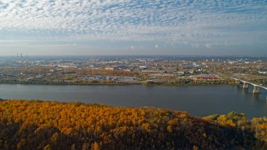 Üzerinden nehir akan ve üzerinde köprü olan bir şehir. Gökyüzü bulutlu ve ağaçlar turuncu. Nizhny Novgorod