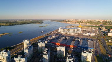Arka planda büyük bir stadyum olan şehir manzarası. Gökyüzü mavi ve su sakin. Nizhny Novgorod