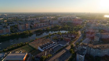 İçinden nehir akan bir şehir manzarası. Gökyüzü güzel turuncu bir renktir. Şehir yüksek binalar ve büyük bir parkla dolu. Nizhny Novgorod