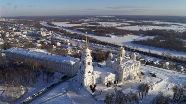 Merkezinde büyük beyaz bir kilise olan karlı bir şehir. Kilise büyük beyaz bir binayla çevrilidir. Gökyüzü mavi ve kar beyaz. Vladimir