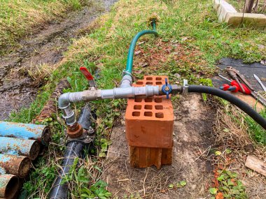 Boru bir tuğlaya ve yeşil bir hortuma bağlı. Tuğla yerde ve hortum boruya bağlı.