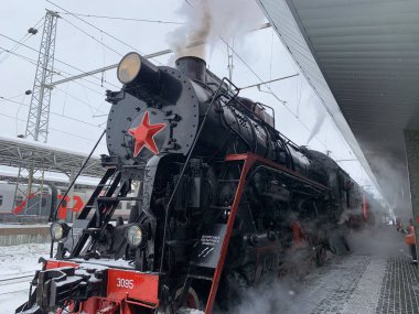 Önünde kırmızı bir yıldız olan tren raylarda oturuyor. Tren siyah ve kırmızıdır ve karla kaplıdır. Trenden çıkan buhar görülebilir.