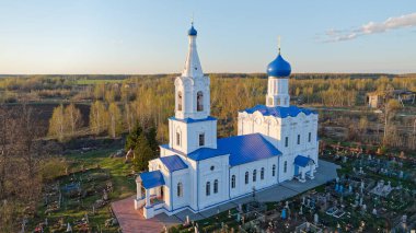 Arkasında mezarlık olan büyük mavi beyaz bir kilise. Mezarlık mezarlıklarla dolu. Kırsal bir mezarlıkta güzel bir taş kilise. Baharın sonlarında gün batımında çekilmiş. Nizhny Novgorod bölgesi.
