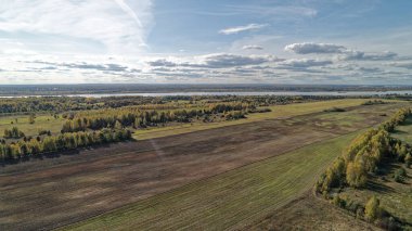 Arka planda nehir olan büyük bir alan. Gökyüzü bulutlu ve güneş parlıyor. Nizhny Novgorod bölgesinde sonbahar ormanı. Rusya.