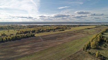 Arka planda nehir olan büyük bir alan. Gökyüzü bulutlu ve güneş parlıyor. Nizhny Novgorod bölgesinde sonbahar ormanı. Rusya.