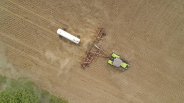 Traktör bir toprak tarlasının içinden geçiyor. Traktör arkasında beyaz bir römork çekiyor. Modern bir traktörle tarımsal alanların amonyak tedavisi. Rusya 'nın Nizhny Novgorod bölgesi.