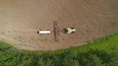 Arkasında büyük beyaz bir tank olan bir tarladan geçen traktör. Modern bir traktörle tarımsal alanların amonyak tedavisi. Rusya 'nın Nizhny Novgorod bölgesi.