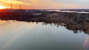 Arkasında şehir olan güzel bir göl. Gökyüzü turuncu ve su sakin.