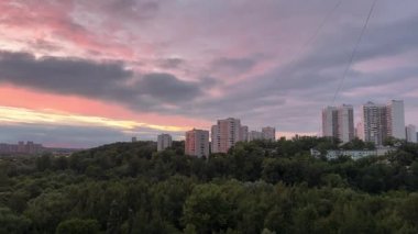 Yüksek binalarla dolu bir şehrin üzerinde güzel bir gün batımı. Gökyüzü bulutlarla dolu ve güneş batıyor. Sıcak ve huzurlu bir atmosfer yaratıyor.