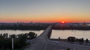 Arka planda günbatımı olan bir nehir üzerinde köprü. Gökyüzü turuncu ve su sakin.
