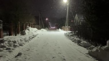 Arka planda sokak lambası olan karlı bir yol. Sokak lambaları karları aydınlatıyor.