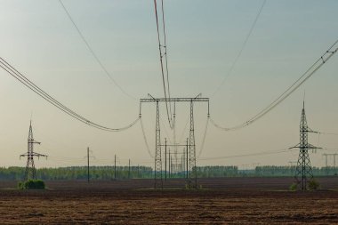 Bir sürü elektrik hattı ve kulesi olan bir alan. Gökyüzü bulutlu ve güneş görünmüyor.