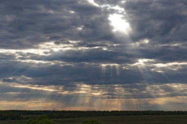 Gökyüzü bulutlu ve güneş bulutların arasında parlıyor. Güneş güzel bir ışık gösterisi yaratıyor.