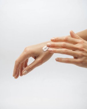 Kadın elleri arka planda beyaz makyaj malzemelerine krem sürerler.