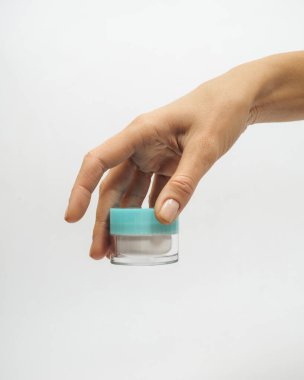 Kadın elleri beyaz arka planda bir kavanoz krem tutuyor.