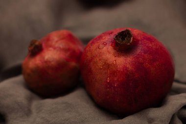 İki sulu ve parlak kırmızı nar gri bir tuvalin üzerinde yatıyor, biri daha büyük, biri biraz daha küçük.