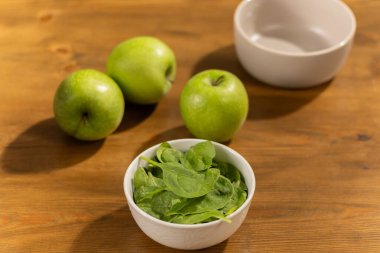 Taze yeşil elmalar ve beyaz kaselerde ıspanak Tahta masa üzerinde yakın plan fotoğraf