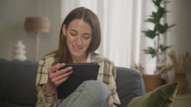 Genç Yetişkin Kafkasyalı Kadın Oturma odasında Tablet Üzerinde Çalışıyor
