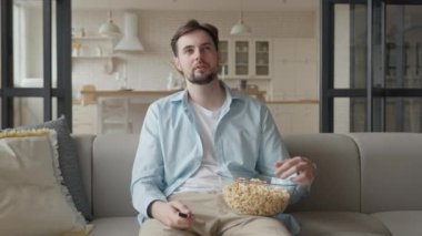 Adam kanepede oturup evde patlamış mısır yiyor.