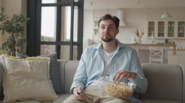 Genç adam film izliyor ve evde patlamış mısır yiyor.