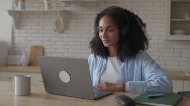20 'li yaşlardaki Afrikalı kıvırcık kadın laptopunda kulaklıkla sohbet ediyor, yüksek kaliteli 4K görüntü.