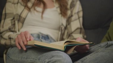Dairesinde kitap okuyan kadın, koltukta otururken kitabı karıştıran kadın.