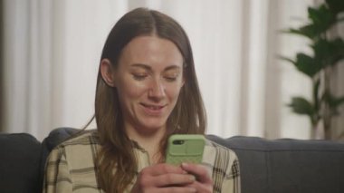 Oturma odasında Koç 'un üzerinde oturan akıllı telefonu kullanan gülümseyen kadın. 