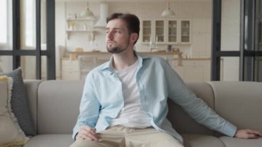 Uzaktan kumandalı yakışıklı beyaz adam oturma odasında oturuyor ve TV seyrediyor, yüksek kaliteli 4K görüntü.