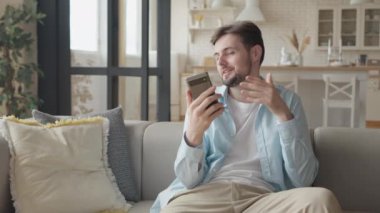  Kanepede oturan beyaz adamı kapatın. Cep telefonuyla görüntülü konuşma yapıyor. Serbest İşadamı Apartman 'da akıllı telefondan video görüşmesi yapıyor.