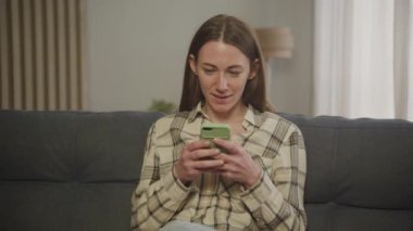 Genç kadın evde koltukta yalan smartphone kullanarak