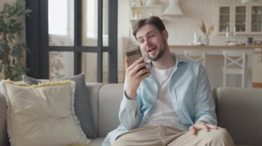 Dairesinde Smartphone 'a video görüşmesi yapan serbest çalışan işadamı, Kanepede oturan beyaz adamı kapatan cep telefonunda görüntülü sohbet yapan, odaklı iş adamı el sallayan eller konferansı
