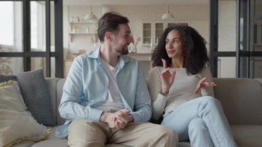 Cozy Sofa 'da oturan ve Oturma Odasında Konuşan Mutlu Genç, Çok Irklı Çift Adam ve Kadın, yüksek kalite 4K görüntüler.