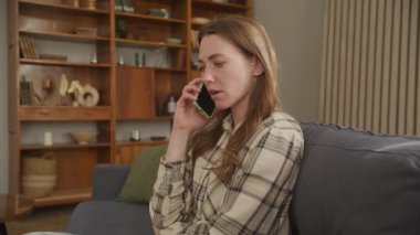 Kanepede otururken telefonda küfreden, Ev Telefonu 'nu arayan kızgın kadın oturma odasında cep telefonuyla konuşan sinirli insanlar. Kafkasyalı Kadın ÜzgünName