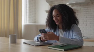 Akıllı Telefon Web Sörf İnterneti ile Mutfakta Dinlenen Afrikalı Kadın, Mobil Uygulamaları Kullanarak Resim Düzenleme, Çevrimiçi Oyun Oynama, Seyahat Rezervasyonu, Bilet Alma. Yüksek kalite 4k görüntü