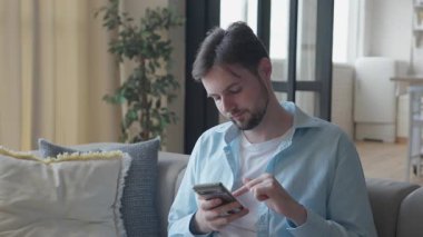 Parlak Modern Yaşam Alanı 'nda dinlenirken Smartphone' da Gündelik Adam Kaydırma, yüksek kalite 4K görüntü