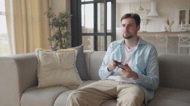 Heyecanlı Adam konsolda video oyunu oynuyor, evde otururken eğleniyor ve kazanıyor. Eğlence, Dijital Eğlence, Neşeli Tepki, Spor, Zafer Anı, Yüksek Kaliteli 4K Görüntü