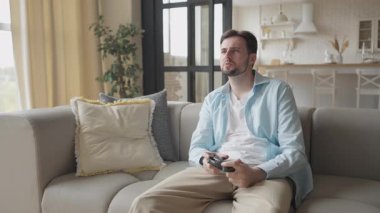 Sinirli adam konsolda video oyunu oynuyor. Mücadele ediyor ve evde kaybediyor. Hayal kırıklığına uğramış Oyuncu, Oyun Başarısızlığı, Dijital Eğlence, Rekabetçi Oyun Oyunu, Duygusal Tepki, Yüksek Kaliteli 4K Görüntüler