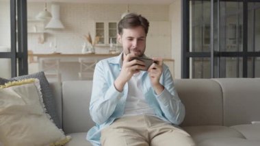 Evde rahat bir koltukta dinlenirken Mobil Oyun Akıllı Telefonu Odaklanan Adam oynuyor. Günlük Oyun, Dijital Eğlence, Eğlence, Girişimci Tecrübe, Etkileşimli Oyun, Yüksek Kaliteli 4K Görüntü