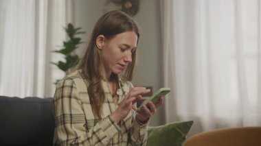 Smartphone 'a sarılıp, haberleri okuyup, evde dinlenen mutlu kadın. Dijital Tarama, Çevrimiçi Bilgi, Sosyal Medya Kaydırma, Günlük Yaşam Taraması, Konforlu Atmosfer, Teknoloji Kullanımı, Boş Zaman