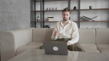 Koltukta otururken dizüstü bilgisayarda çalışan genç beyaz adam. Odaklanmış Profesyonel, Uzaktan Çalışma, Modern Ofis, Dijital İş, Üretim, Teknoloji, İş Stratejisi, Konforlu Çalışma Alanı
