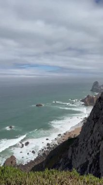 Portekiz 'de Rocky Shore' a çarpan dalgalarla çarpıcı bir uçurum manzarası. Görkemli Sahil Manzarası Nefes Kesen Manzarası, Engebeli Kayalıklar ve Bulutlu Gök Altında Güçlü Okyanus Dalgaları