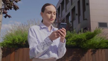 Açık havada duran genç iş kadını, Smartphone 'a odaklanmış, Önemli Haberleri Ciddi İfadeyle Okuyor, Dijital İletişim, Modern Profesyonel Yaşam Tarzı. Yüksek kalite 4k görüntü