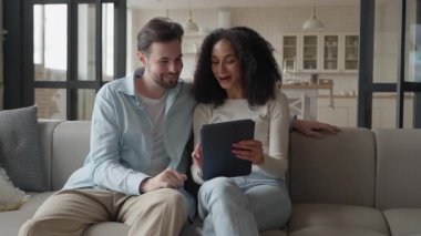 Koltukta oturan gülümseyen bir çift, rahat evlerinde tablette birlikte olmanın tadını çıkarıyorlar. Yüksek kalite 4k görüntü