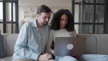 Odaklanmış çift dizüstü bilgisayarları karıştırıyor, evde ciddi şeyler tartışıyorlar. Derin bir sohbete dalmış, modern oturma odasında rahatça otururken kararlar veriyor. Yüksek kalite 4k görüntü