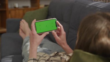 Soğukkanlı Kadın Yeşil Ekranlı Akıllı Telefon 'u kullanarak rahat bir şekilde koltukta uzanıyor. Model, Teknoloji Konseptleri, Sosyal Medya, Yayıncılık ve Rahatlama İçin Mükemmel. Yüksek kalite 4k görüntü