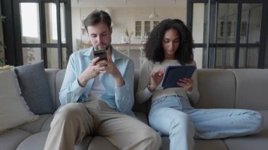 Çift koltukta dinleniyor, aletlerine odaklanıyor, akıllı telefonlara ve tabletlere bakıyor. Modern Teknoloji Yaşam Tarzı, Dijital Bağlantı, Konforlu Ev Ayarları, Gündelik Etkileşim, Sosyal Medya Taraması