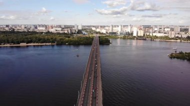 Kyiv 'deki Hava Manzaralı Paton Köprüsü, Dinyeper Nehri üzerindeki şehir trafiğini yakalıyor. İkonik Köprü 'yü gösteren çarpıcı İHA görüntüsü, Akan Arabalar, Sudaki Yansımalarla Nefes Kesen Şehir
